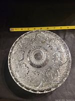 Top view of the round pressed glass candy dish showing the detailed pattern and measuring tape indicating about 8 inches diameter.