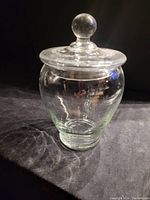 Clear vintage candy jar with a rounded body and a round knob on the lid.