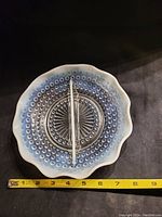 Top down image of vintage carnival glass serving plate showing hobnail texture, ruffled edge and metal handle with measuring tape indicating width.