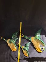 Set of three vintage chalkware ducks with measuring tape showing size. Ducks are green, yellow and brown with imperfections.