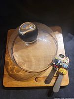 Top view of wooden cheese serving tray with glass dome lid and two decorative spreaders with character handles