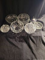 Photo of seven vintage crystal glass dishes including candy dishes with lids and serving bowls, showing intricate cut glass patterns and reflective clear glass.