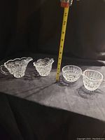 Two pairs of crystal glass cream and sugar containers displayed with measuring tape showing height 3-4 inches