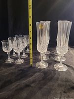 Shows two groups of clear crystal glasses, 6 taller and 6 shorter, against dark background with measuring tape showing height of the tall glasses over 7 inches.