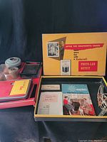 Top-down photo showing the open Kodacraft Photo-Lab Outfit box with visible manuals, chemical box, and accessories inside.