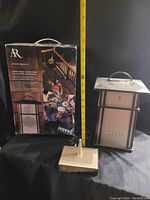 Full view of AR outdoor speaker and its box alongside remote control and measuring tape showing height approx 12 inches.