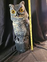 Plastic owl figurine on dark background with measuring tape showing height approximately 16 inches