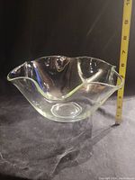 Photo of large clear glass salad bowl taken from the side showing wavy scalloped rim and measurements with a ruler indicating height about 7 inches.