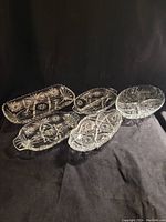 Group of five vintage clear glass serving dishes with ornate pressed starburst and floral patterns under lighting on black backdrop.