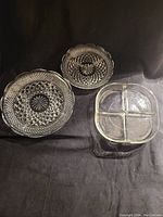 Photo of 3 glass serving dishes on black fabric background: two round patterned plates of different sizes and one square divided dish