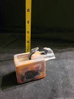 Small wooden sculpture of snake emerging from box with carved fish detail, shown next to measuring tape for height around 3 inches.