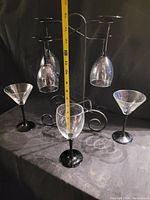 Three vintage-style wine glasses with black stems and bases on a black table with a black metal curved stand holding some glasses upside down. Measuring tape shows approximate size.