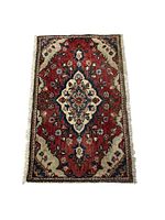 Full view of a small rectangular Hamadan wool rug with a red field and central medallion pattern, showing borders and fringed edges.