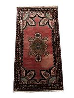 Full top view of a small rectangular rug with geometric medallion and floral border in natural shades of wool colored pink, green, black and beige.
