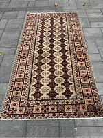 Full view of the rectangular Persian Turkmen rug laid on a paved surface showing detailed floral and geometric patterns with a white background.