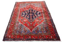 Full view of rectangular Zanjan wool rug with red field, central navy medallion, corner spandrels, floral borders and fringes