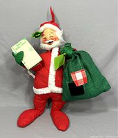 Front view of the 17-inch tall red plush Santa doll with white trim, green sack, and holding a list.