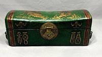 Front view of antique Chinese wooden box showing green paint, gold characters, and brass clasp lock.
