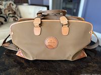 Front view of brown Lancel duffel bag showing leather patch logo and tan leather trim and handles.