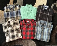Six men's long sleeve shirts folded on carpet in various patterns and colors including plaid and solid, size Large.