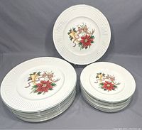Photo showing the full set of white ceramic holiday plates with Christmas design, separated into dinner and salad plates stacks and one plate on stand with visible festive pattern.