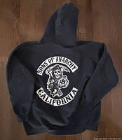 Back view of black Sons of Anarchy hoodie showing large white graphic of grim reaper holding a scythe with text 'Sons of Anarchy' and 'California'.