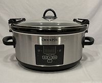 Front view of the oval stainless steel Crock-Pot slow cooker with glass lid and handles on sides.