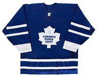 Front view of the blue Toronto Maple Leafs CCM hockey jersey with white stripes and white tackle twill crest showing the Doug Gilmour autograph on the crest.