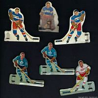 Six metal hockey player pieces arranged on a black background, showing front view with painted player illustrations and metal bases.