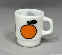 Side angle view of the white milk glass mug featuring one large orange peach graphic with a green leaf and black outline, showing the handle and pedestal base.