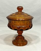 Full front view of the amber glass candy dish on pedestal, showing lid and round knob, embossed thumbprint pattern, and decorative base