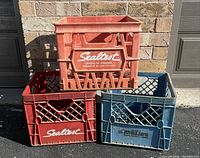 Three vintage plastic milk crates stacked: two red and one blue, all with Sealtest branding, showing dirt and wear.