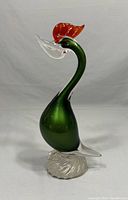 Side view of Murano glass bird figurine showing green body, clear beak, red comb, and clear swirled base.