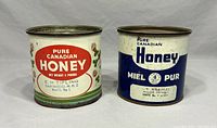 Front view of two vintage Pure Canadian Honey metal tins side-by-side showing labels and details with rust visible