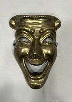 Front view of the solid brass comedy mask showing detailed facial features and shiny surface.