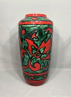 Full front view of the tall pottery vase showcasing the red and green floral pattern and the glazed ceramic surface.