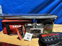 Photo showing lot contents including booster cables in soft case, 1.5 Amp battery charger box, Smart Repair fluid container, red roadside assistance bag, and folded sun shade