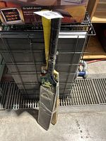 Photo showing two used cricket bats with black/yellow and yellow grips placed together leaning on a metal surface.