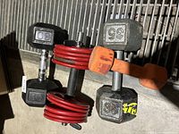Photo showing two black 30 lb hex dumbbells, one orange 8 lb dumbbell, two grey 35 lb hex dumbbells, and one adjustable dumbbell with red plates.