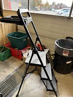 Side view showing the metal ladder open with three steps and a handle at the top with the work tray.