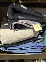 Stack of three furniture moving blankets folded, colors black, gray, beige, and blue visible