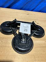 Top view showing the suction plate with three connected suction cups and a metal handle in the center, placed on a wooden surface with a blue backdrop.