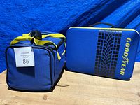 Photo of two Goodyear automotive safety kits in blue and yellow fabric bags, one with tire tread design and logo, side by side.