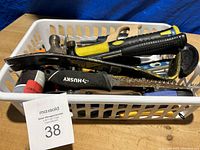 Photo showing a plastic basket filled with used hand tools including hammers, saws, clamps, screwdrivers, a level, and adhesive bottle.