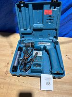 Blue Makita cordless drill with attached battery pack, charger with cord, and additional cylindrical battery pack inside an open blue plastic carrying case.