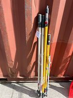 Full view of all painting poles leaning against a red container showing length and some wear.