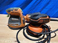 Photo of the two palm sanders, Ridgid cordless model on left and Black & Decker corded model on right showing overall condition and cord