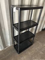 Front view of black plastic storage shelf with three levels, showing overall condition and structure.