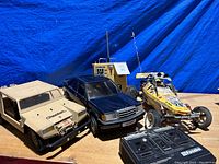 Wide shot showing three RC vehicles, two remotes, and parts box all dusty