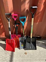 Five small snow shovels arranged side-by-side showing handles and blades, variety of colors and designs.